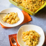 Two white bowls of butternut squash mac and cheese with orange napkins and a green casserole in the background.