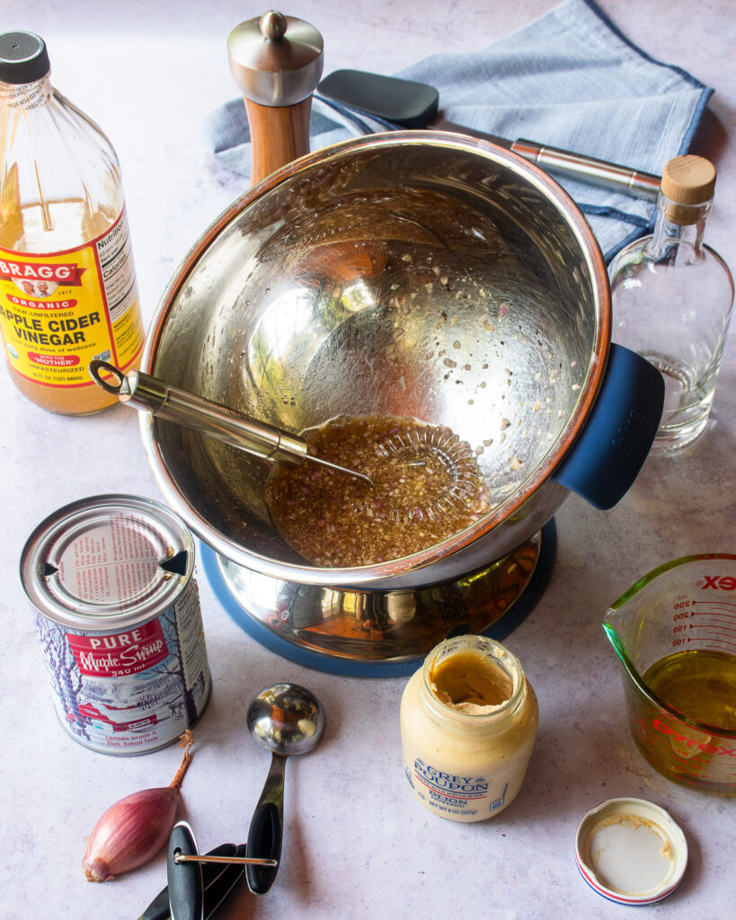 Ingredients for the dressing for farro salad in a bowl with jars and tablespoon measures near by.