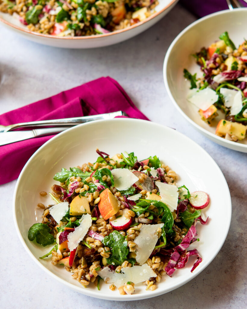 A shallow white bowl with farro salad in it and a pink napkin with utensils next to it.