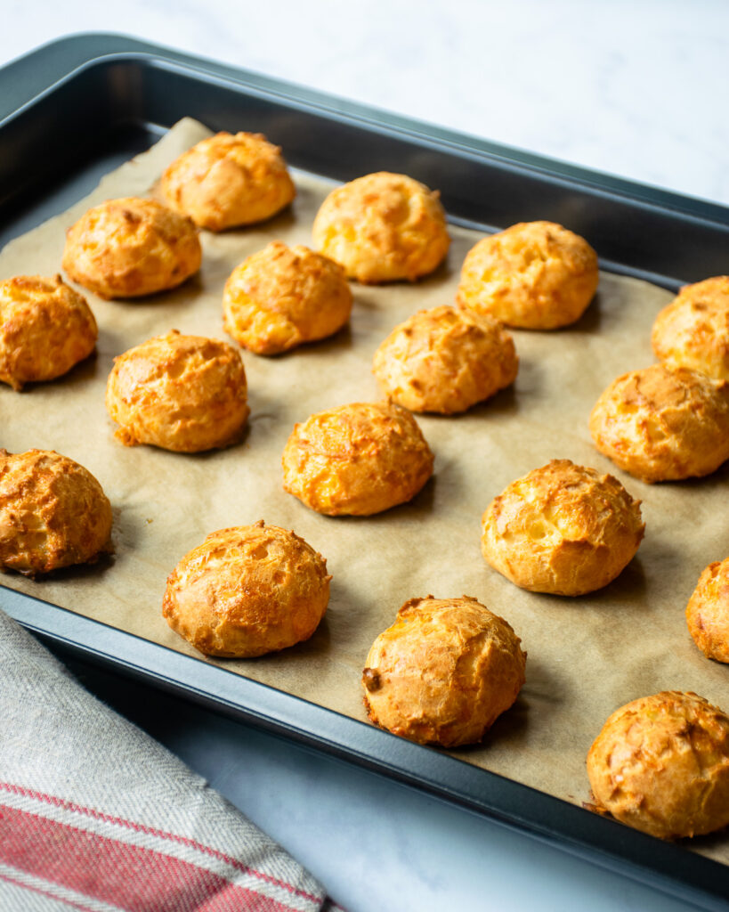 Gougères on a baking sheet, lined with parchment.