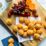 Gougères on a cutting board with some fruit and wine nearby.