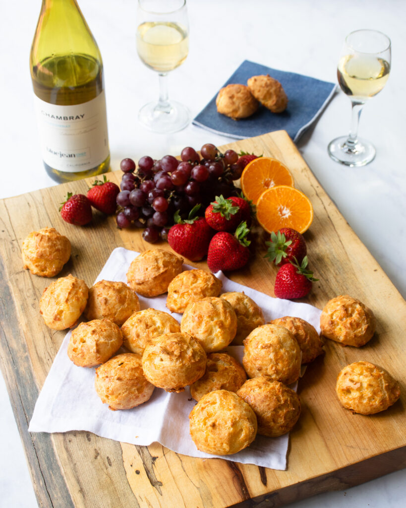 Gougères on a wooden board with fruit and wine.