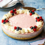 A no bake layered cheesecake on a blue countertop with a stack of plates behind it.