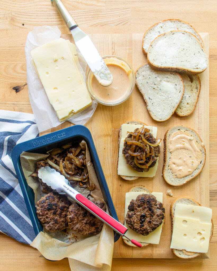 Assembling patty melts with rye bread slices, burger sauce, cooked burger patties and Swiss cheese.