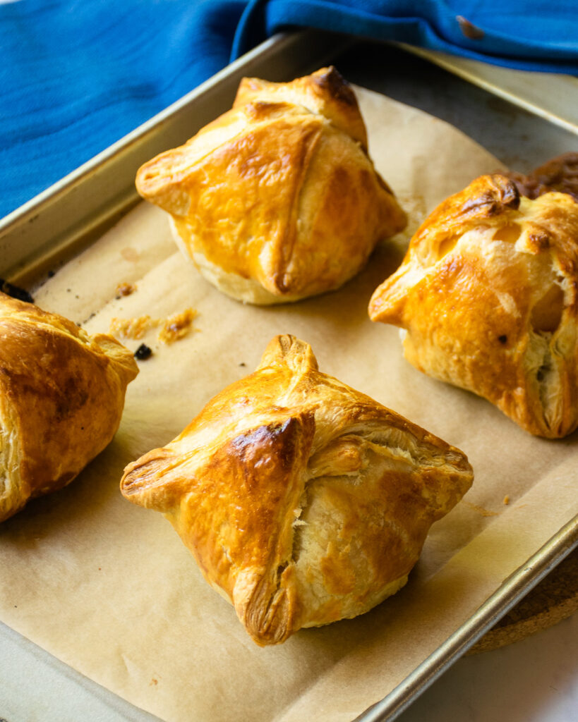 Baked peach dumplings on a parchment paper lined baking sheet.