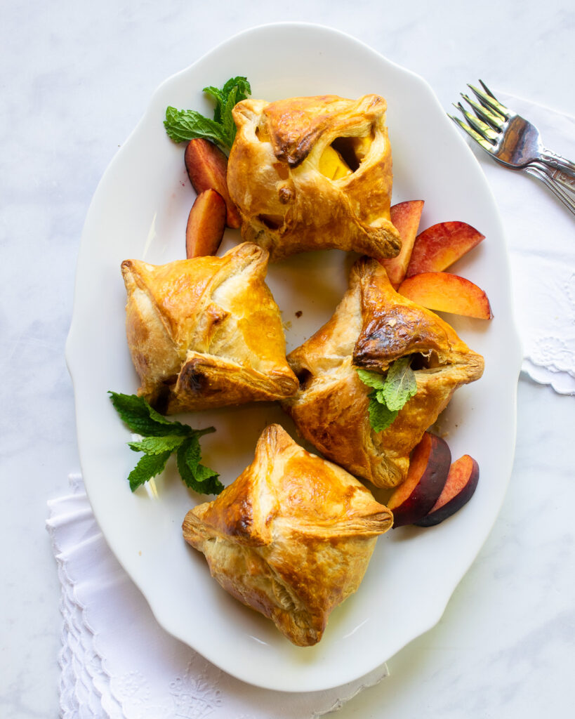 Looking down on four peach dumplings with peach slices and mint, all on a white oval platter.