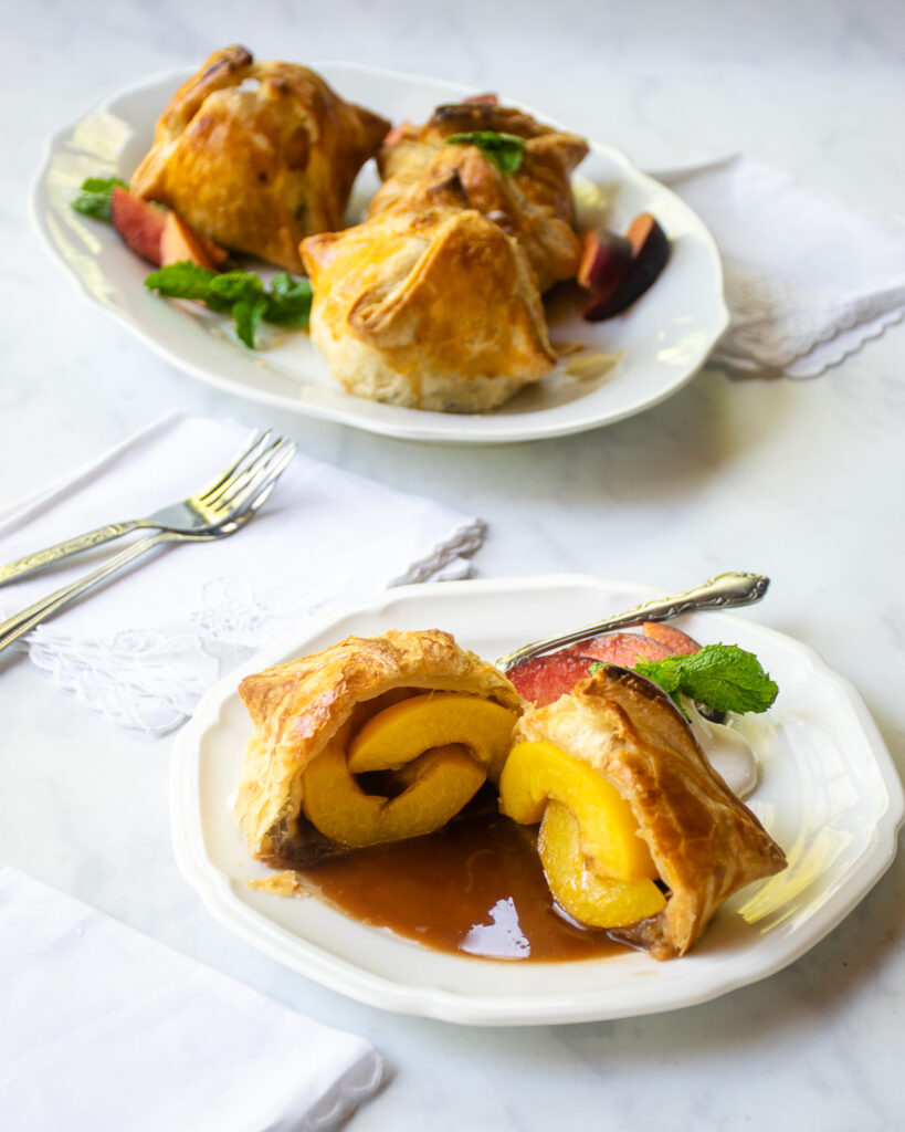 A small white dessert plate with a peach dumpling cut in half, with more dumplings in the background.