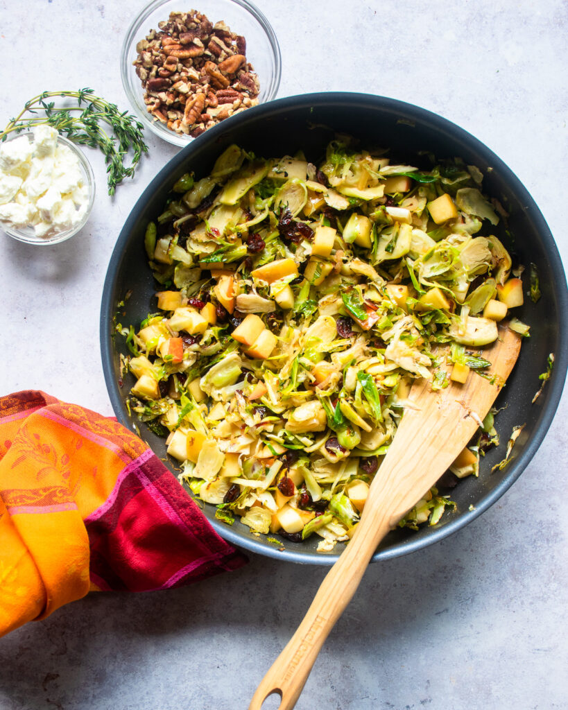 Apples, Brussels sprouts and dried cranberries in a skillet with a wooden spoon.