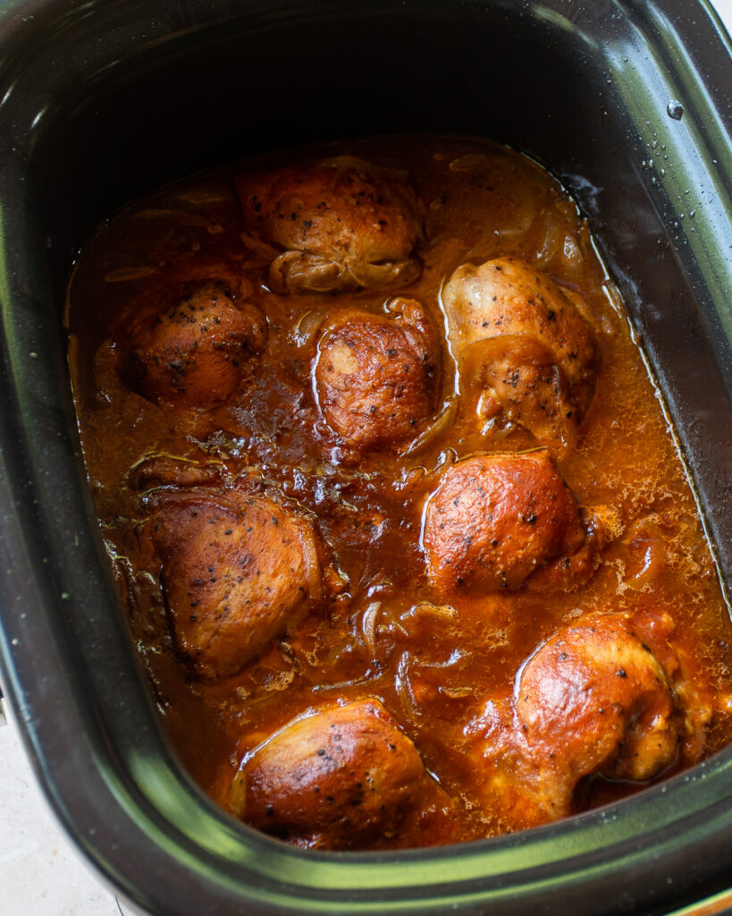 Looking down into a slow cooker with slow cooked BBQ chicken thighs inside.