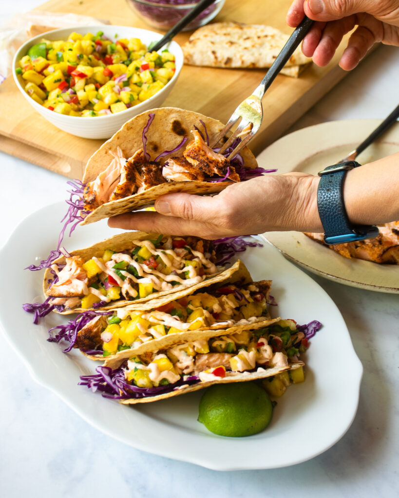 Hands building spicy salmon tacos over a platter.