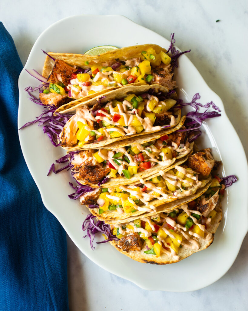 An oval white plate with five spicy salmon tacos next to a blue napkin.