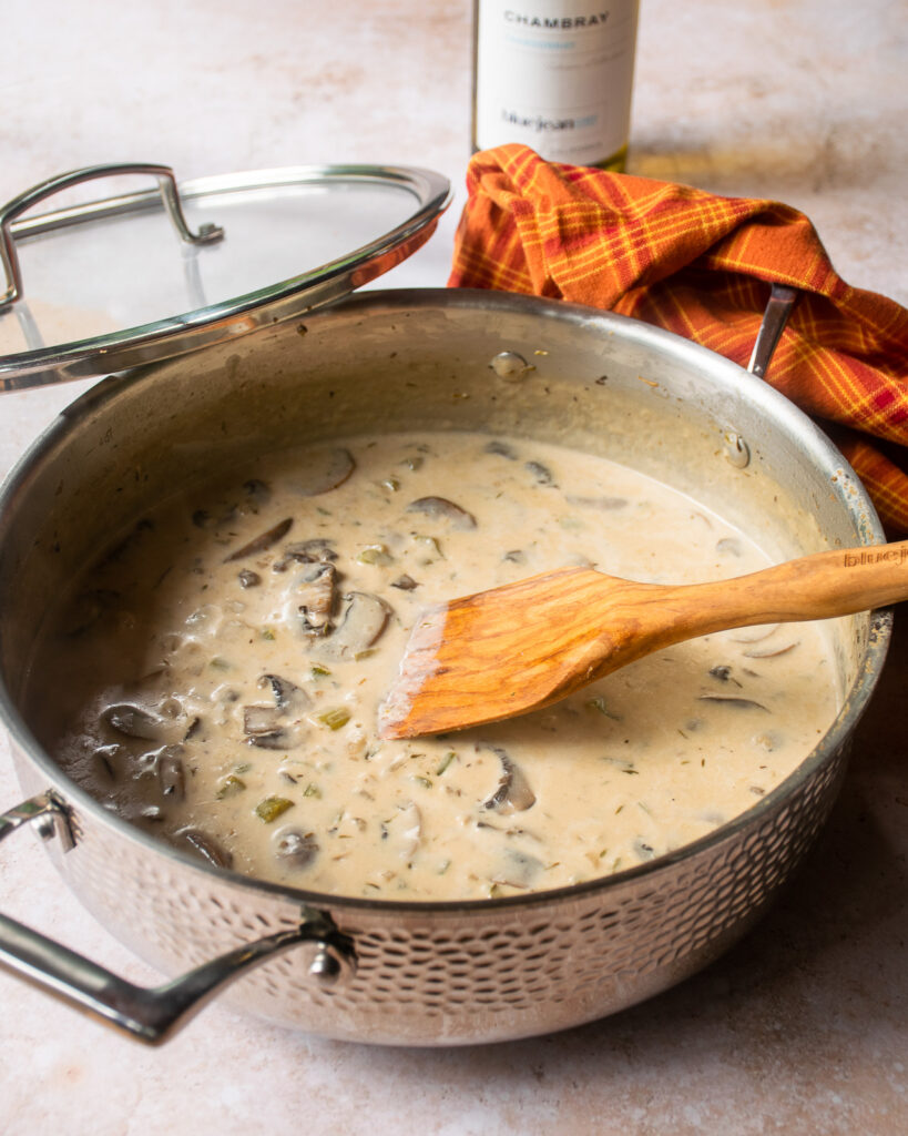 A mushroom sauce in a stainless steel saute pan with a wooden spoon sticking out of it.