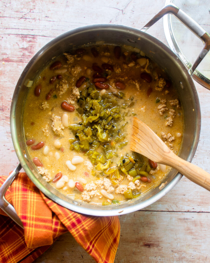 Looking down into a soup pot with white chicken chili and canned Jalapeños on top.