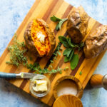 Looking down on a baked sweet potato with butter inside and herbs around.