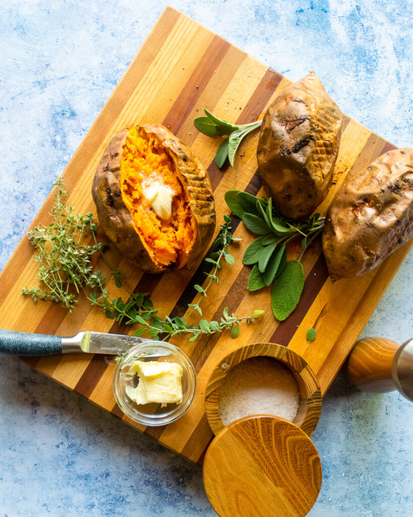 Looking down on a baked sweet potato with butter inside and herbs around.