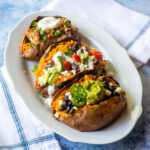 An oval white plate with three baked sweet potatoes with different stuffing in each one.