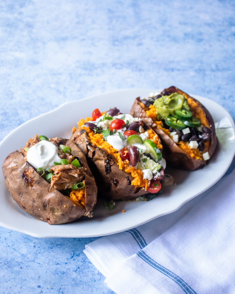 An oval white plate with three baked sweet potatoes with different stuffing in each one.