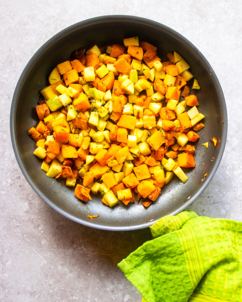 Butternut squash and apple in a blue non-stick skillet with a green towel wrapped around the handle.