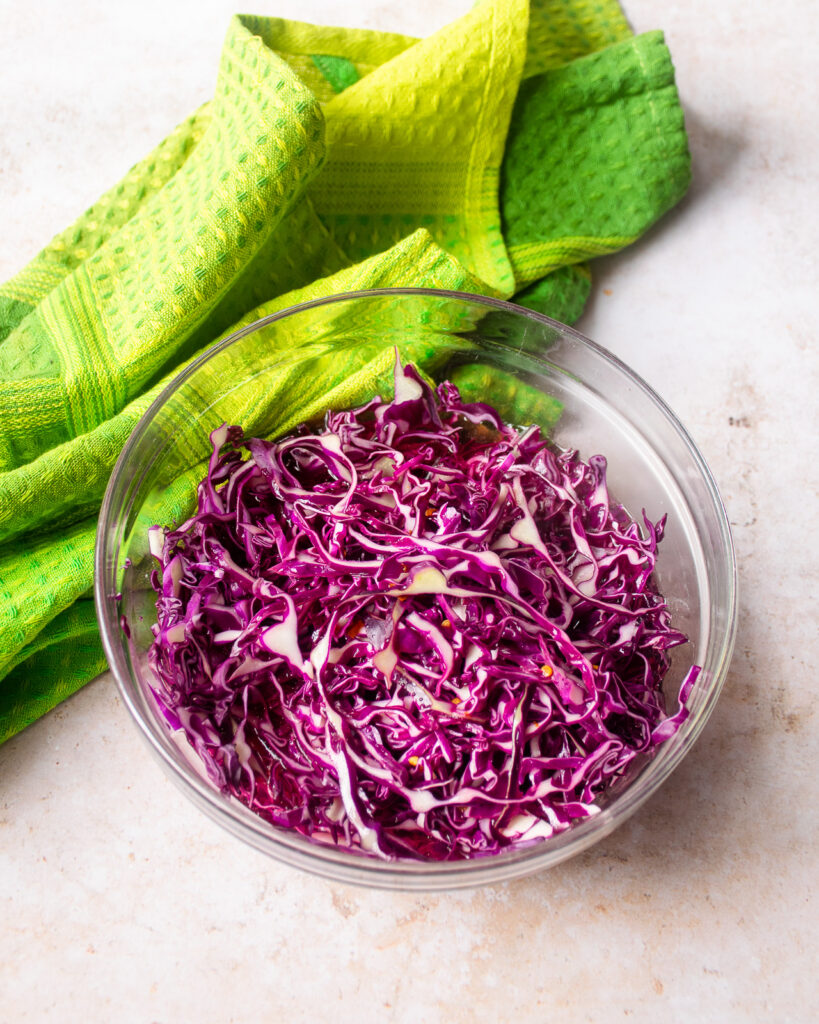 a glass bowl of pickled red cabbage with a green kitchen towel