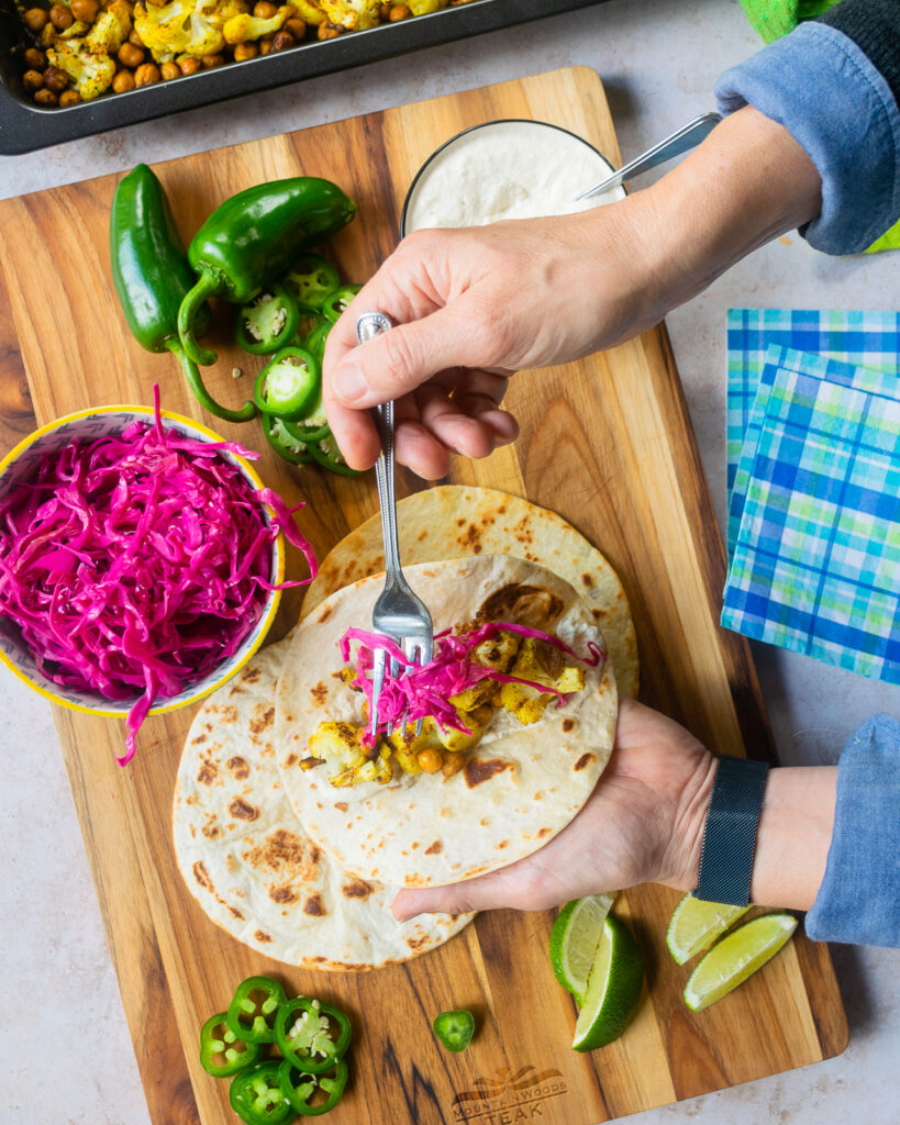 Hands building a cauliflower taco with cashew crema and pickled red cabbage.