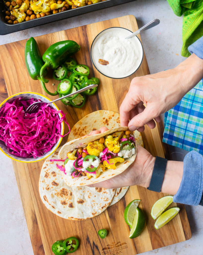 Hands holding a filled cauliflower taco over a taco station.