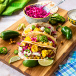 Cauliflower tacos on a cutting board with ingredients around.