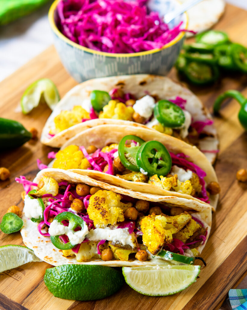 Cauliflower tacos on a cutting board with ingredients around.