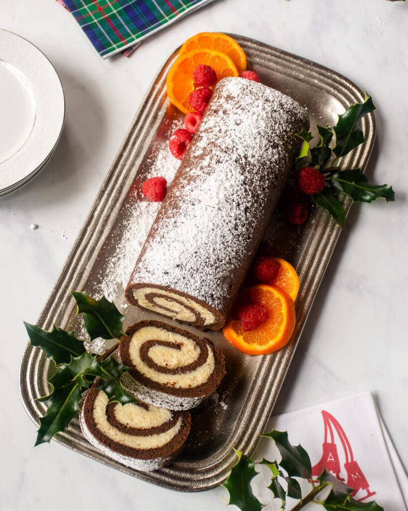 Looking down on a chocolate Swiss roll coated with powdered sugar and a couple of slices cut.