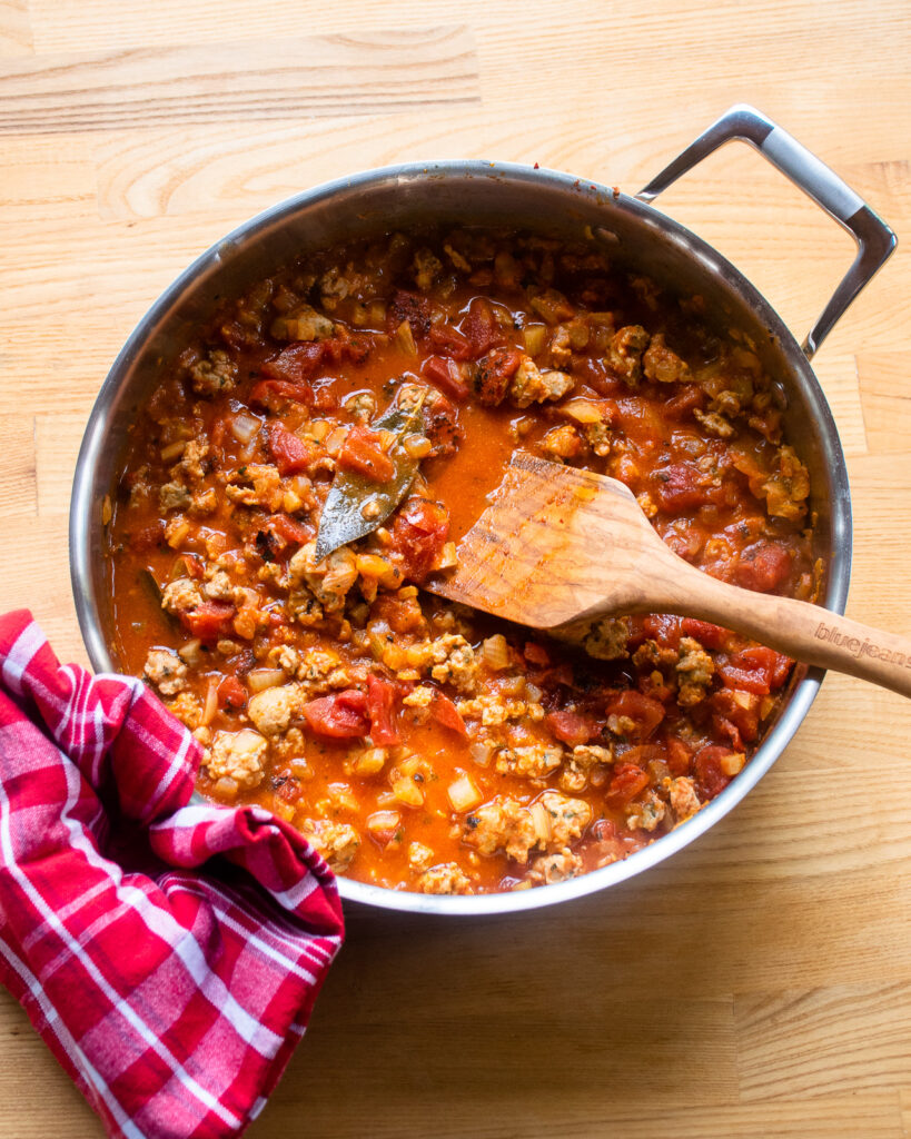 Looking down into a saute pan with chicken bolognese sauce and a wooden spoon sticking out of it.