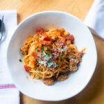 Looking straight down into a white bowl of spaghetti with chicken bolognese sauce.