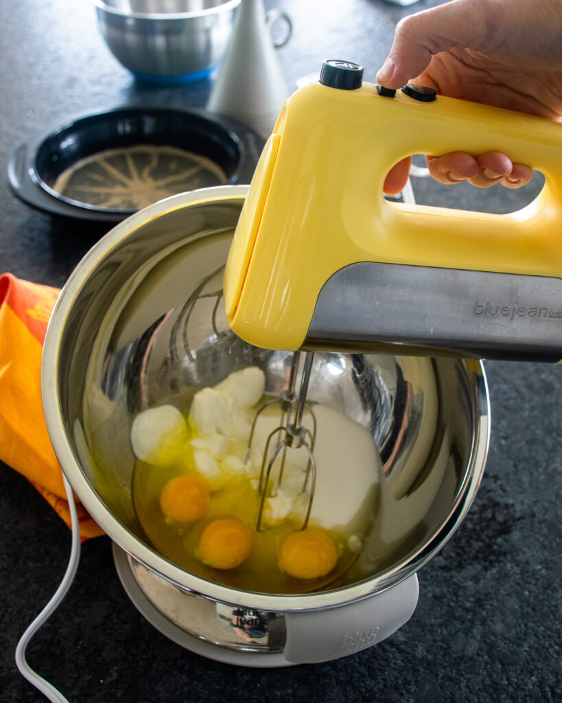 A yellow hand mixer about to mix ingredients in a stainless steel bowl.