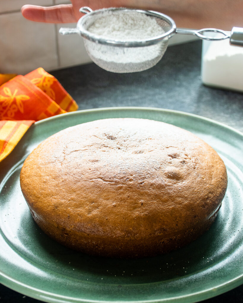 Dusting a cake with powdered sugar on a green platter.