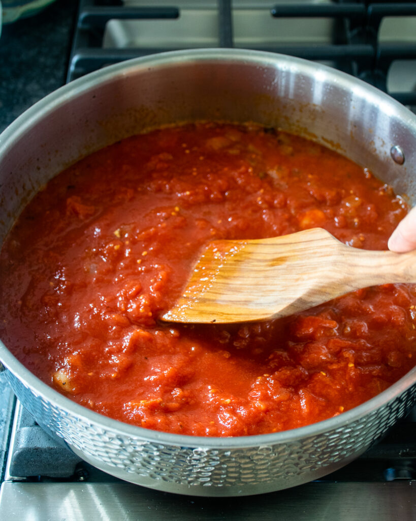 Amatriciana sauce simmering in a stainless steel saute pan with a wooden spoon sticking out.