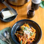 Pasta amatriciana in a black pottery bowl on a wooden table with a place setting and wine.