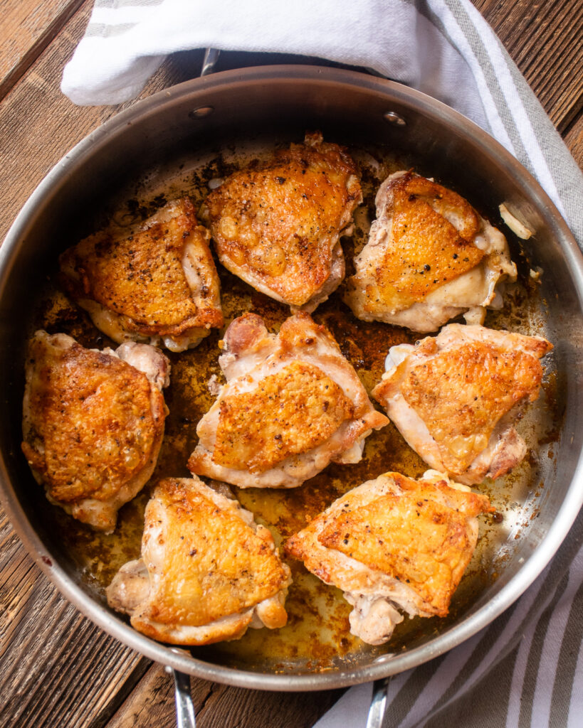 Chicken thighs browned in a stainless steel saute pan.