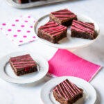 Squares of chocolate raspberry brownies on various different plates.