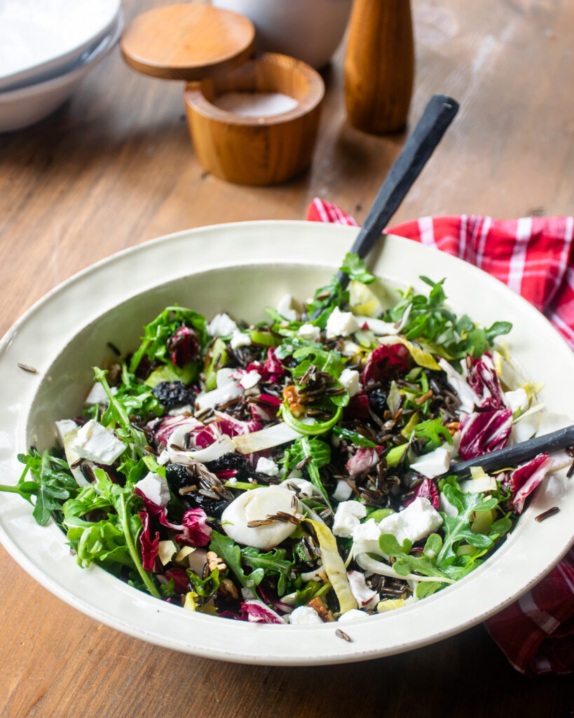 Wild rice salad in a white bowl with salad servers sticking out.