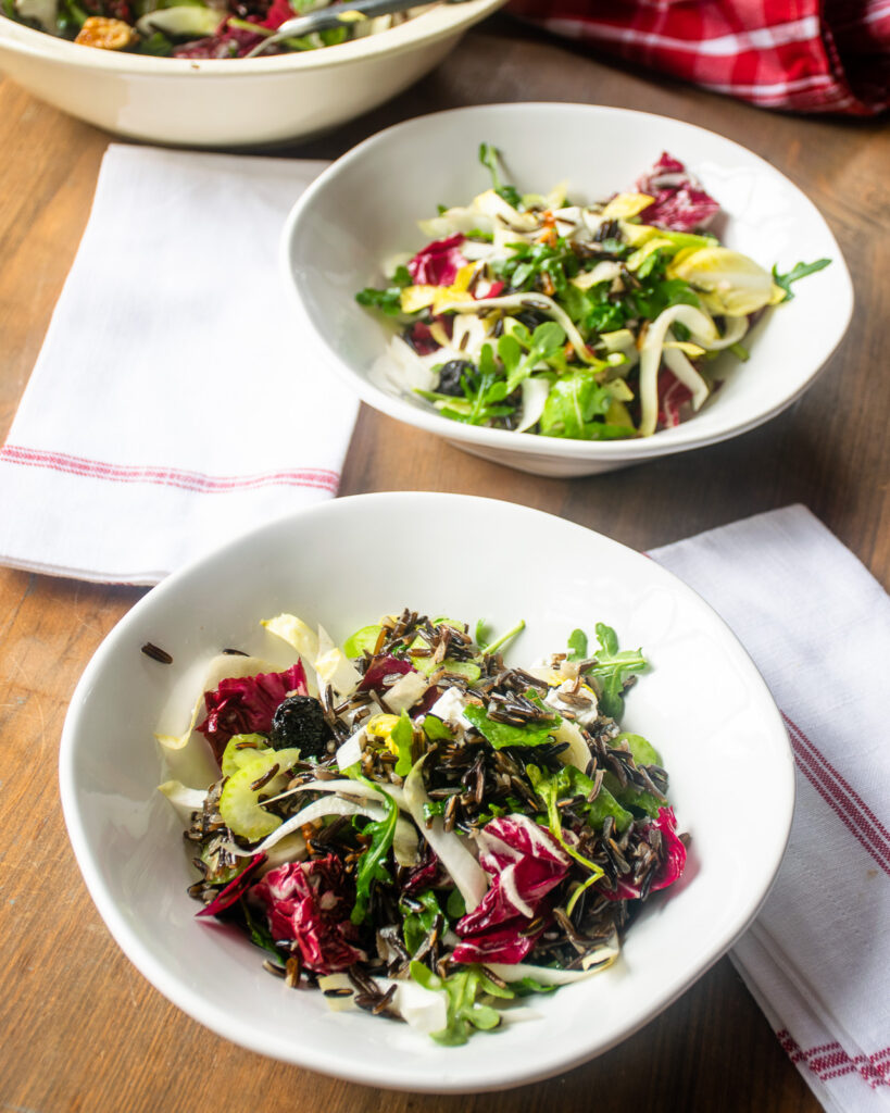 Two bowls of wild rice salad in front of a salad bowl of the same.