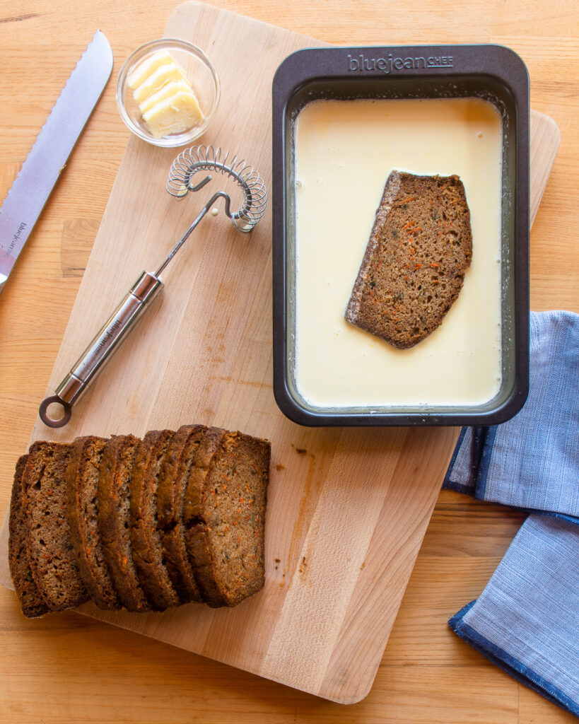 A slice of carrot cake loaf soaking in a baking pan of egg batter.