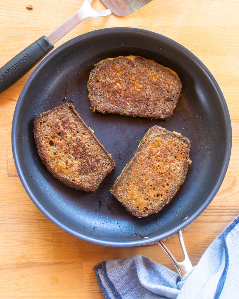 Looking down into a skillet with 3 slices of carrot cake french toast cooking in it.