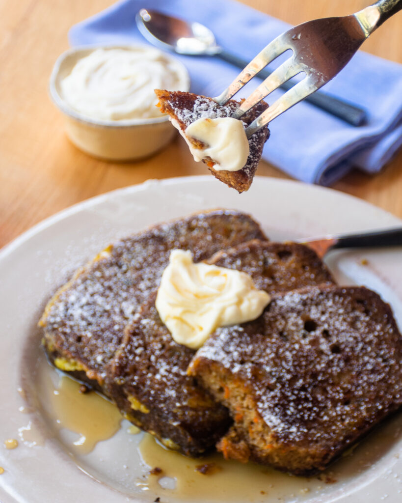 A fork holding a piece of carrot cake french toast above a plate of the same.