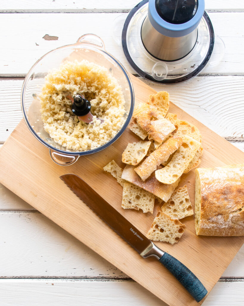 Looking down into a food chopper with breadcrumbs next to a bread knife and some bread crusts.