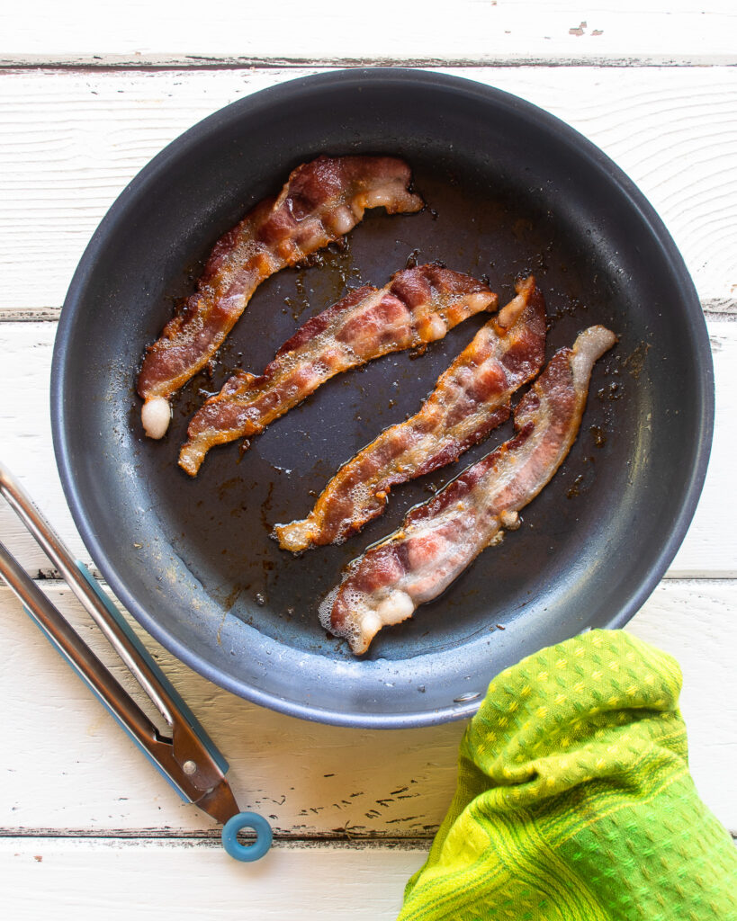 Looking down into a blue non-stick skillet with four rashers of bacon inside.