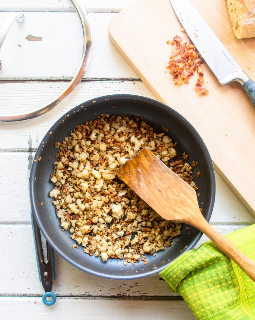 Looking down into a skille with a wooden spoon sticking out of it, breadcrumbs inside.