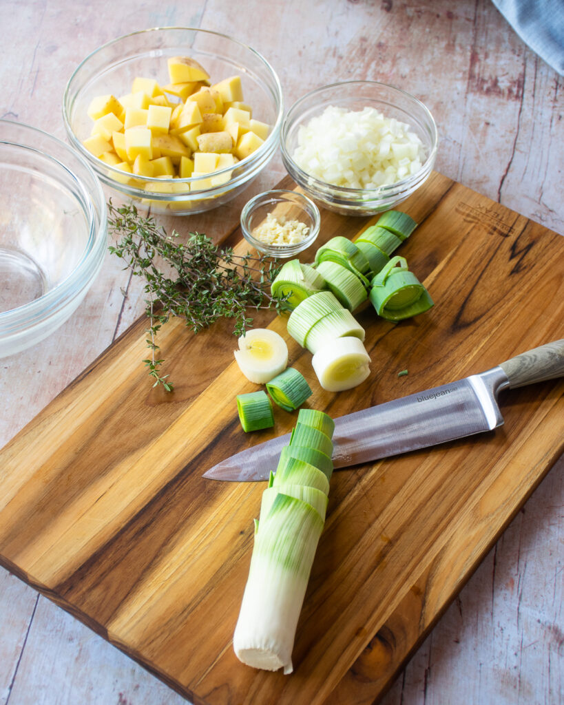 A cutting board with a knife and a leek being sliced into rounds.