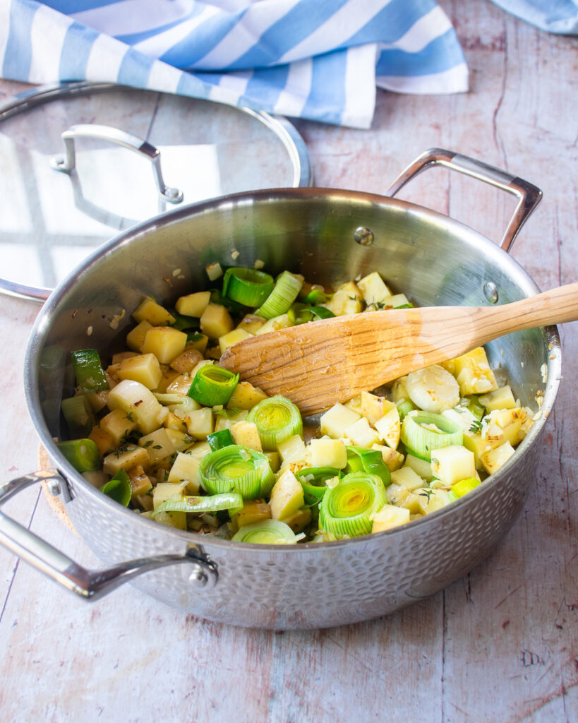 A saute pan and wooden spoon with sautéed vegetables inside.