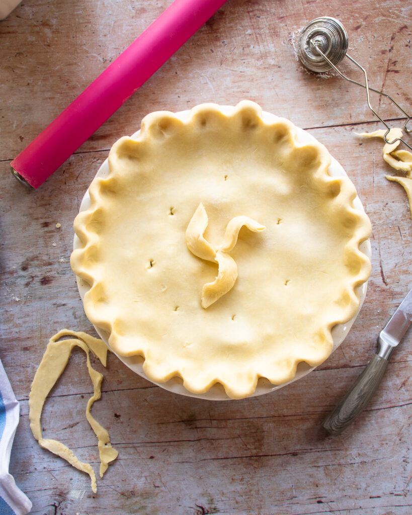 Looking down on an unbaked ham leek and potato pie with a pink rolling pin near by.