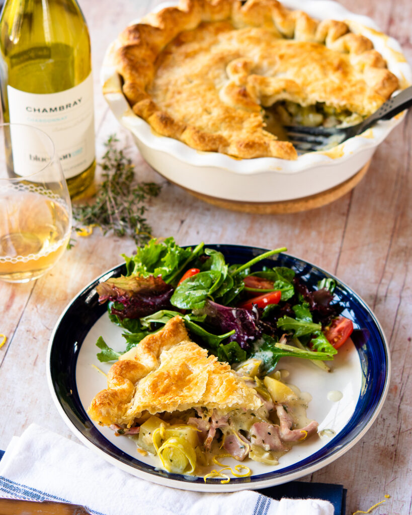 A blue rimmed plate with a piece of ham leek and potato pie and some salad.