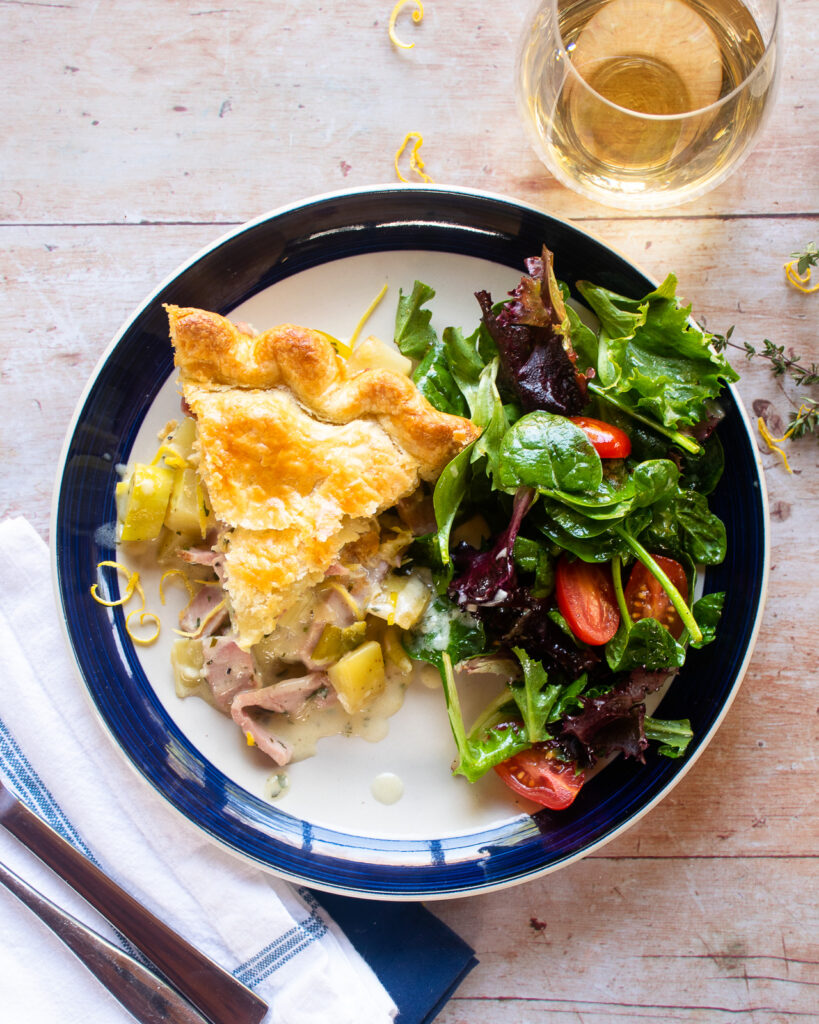 A blue rimmed plate with a piece of ham leek and potato pie and some salad.