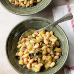 A green ceramic bowl with white beans and ham and a spoon sticking out.